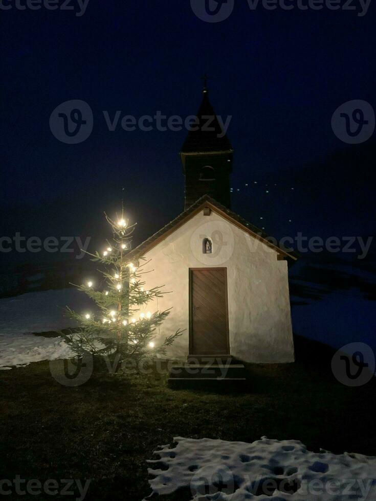 små kapell med ett upplyst jul träd på natt i de bavarian alps foto