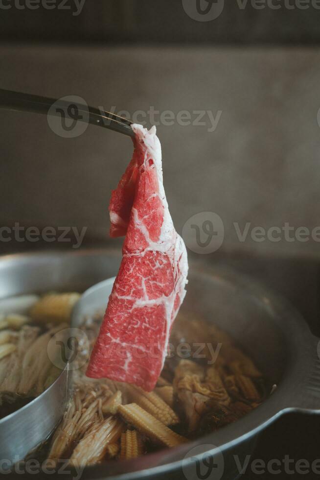 rå nötkött och dopp den i en kokt soppa på en varm pott. shabu shabu japansk mat stil. foto