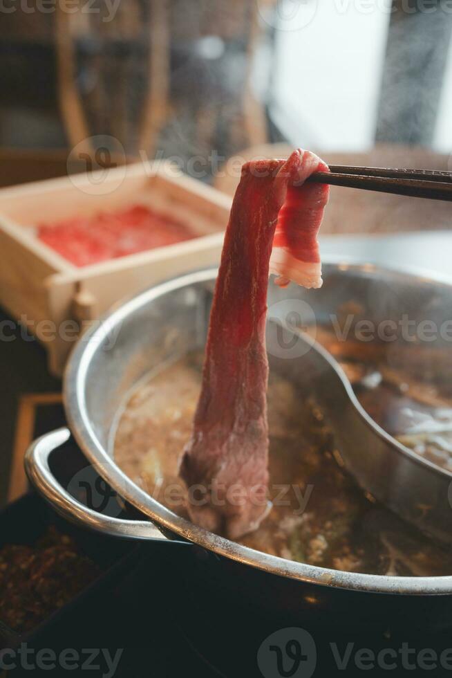 doppning en skivad bit av fläsk in i vatten varm pott under äter shabu eller sukiyaki måltid. foto