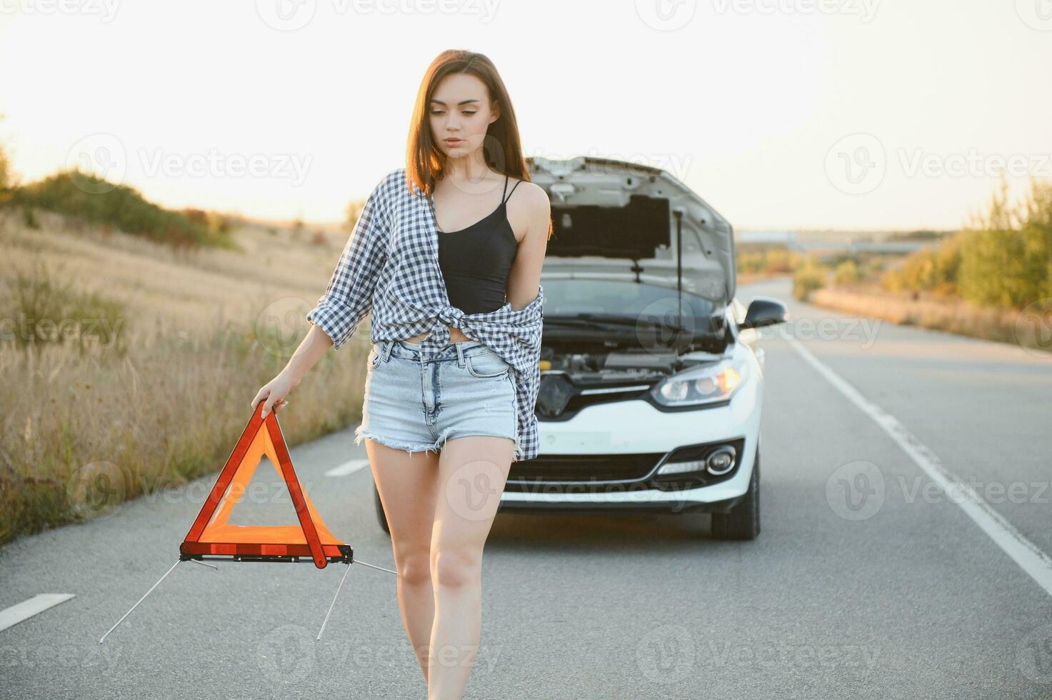 skön sexig kvinna innehav ett nödsituation sluta tecken nära en bruten bil. foto