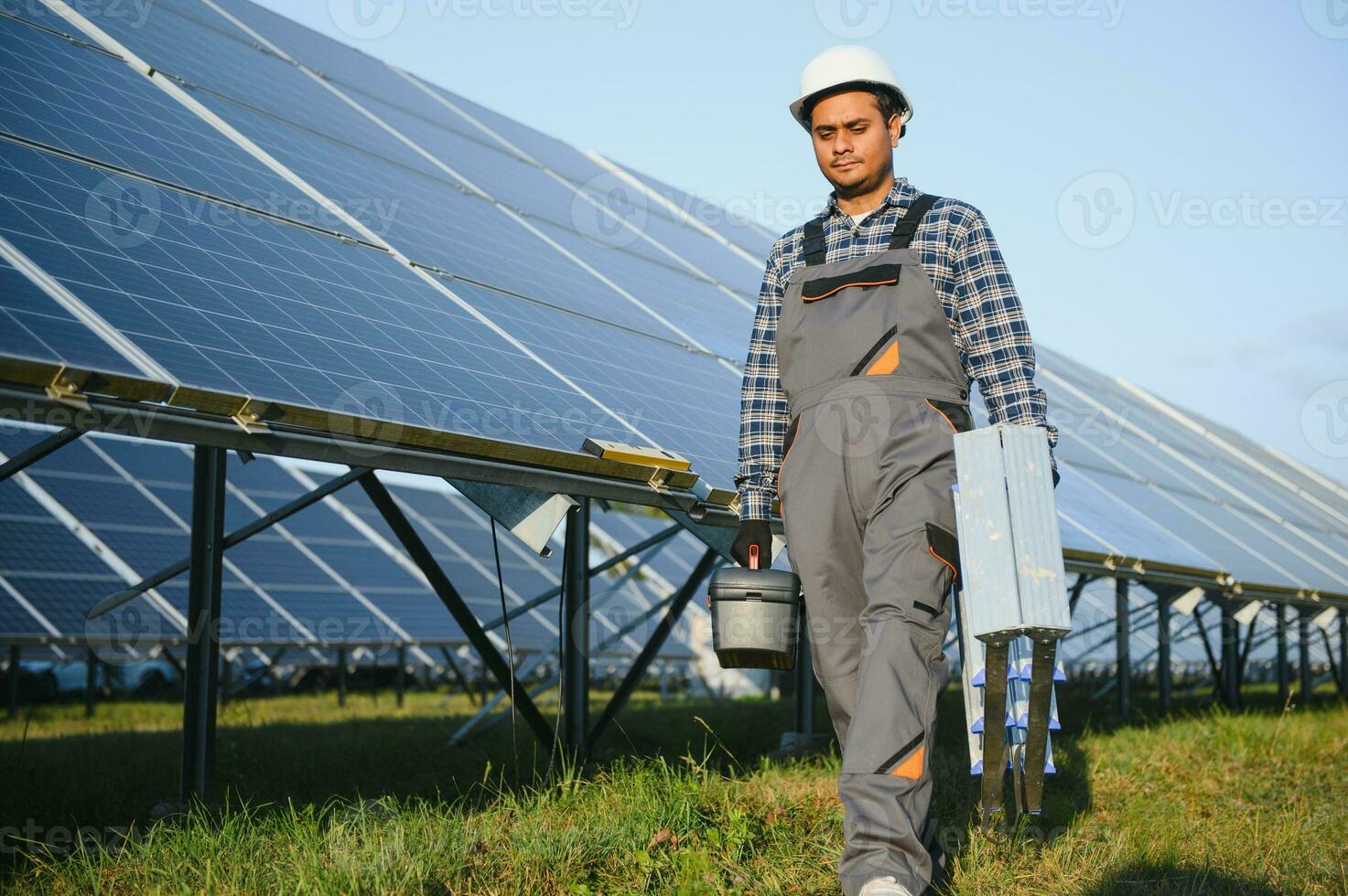 indisk man i enhetlig på sol- odla. behörig energi ingenjör kontrollerande arbete av solceller celler foto