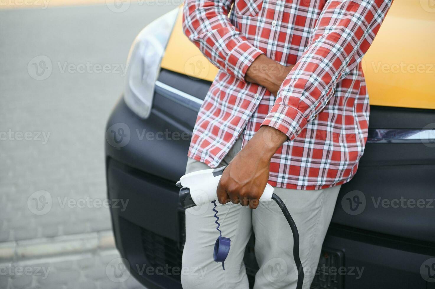 afrikansk man innehav avgift kabel- i på hand stående nära elektrisk bil. foto