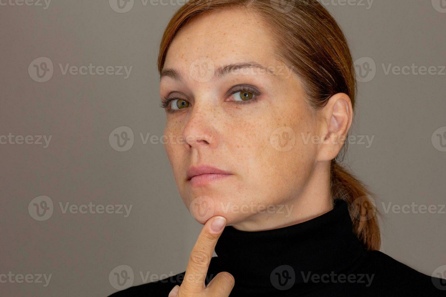 porträtt av beskurna caucasian mitten åldrig kvinna ansikte med fräknar rörande haka förbi finger foto