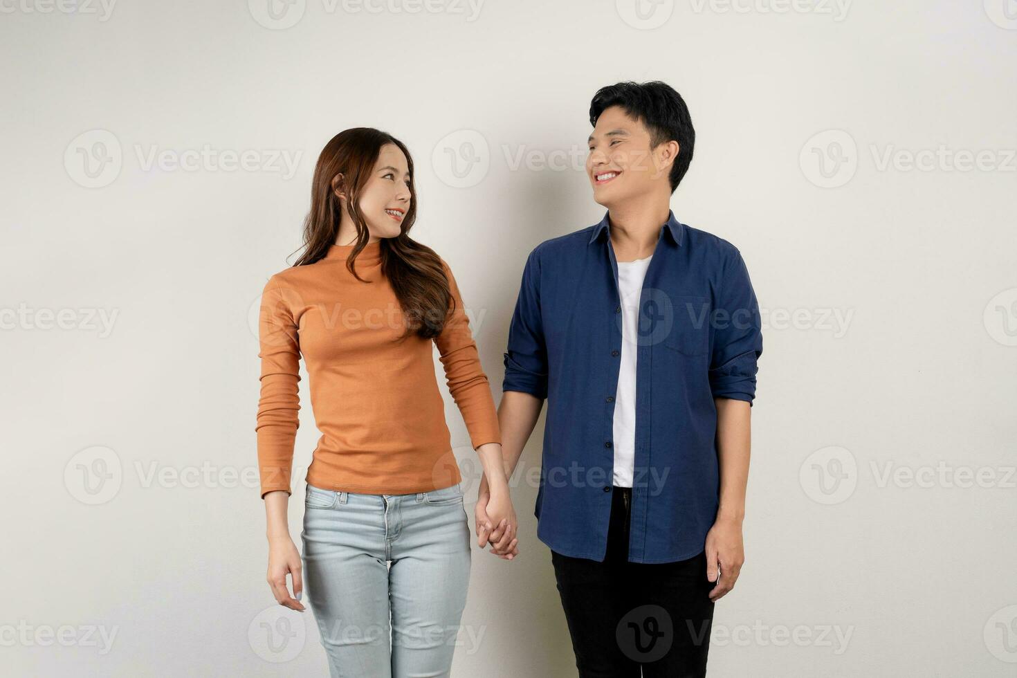 glad ung asiatisk par i tillfällig klädespersedlar leende och ser på varje Övrig med innehav händer. man och kvinna varelse i kärlek foto
