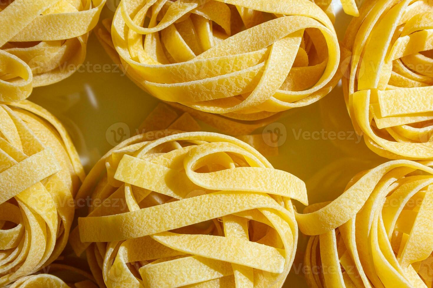 okokt äggbaserad fettuccine pasta. en kulinariska duk av bandformad makaroner, skapande en livlig och texturerad bakgrund för gourmet matlagning. torr pasta. rå makaroner - topp se, platt lägga foto