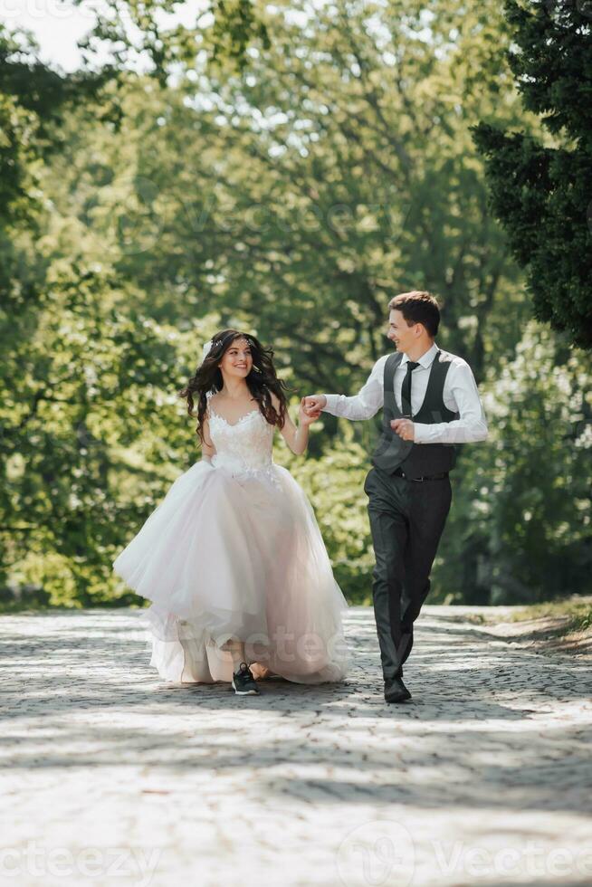 brudgum och brud i de trädgård. vår bröllop i de parkera. Lycklig bröllop par löpning i de parkera. eleganta och skön. prinsessa klänning. foto