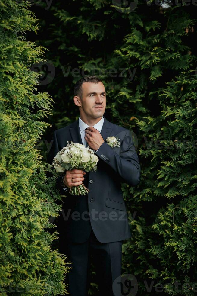 en man i en svart kostym poser i natur med en bukett. en eleganta Kolla på. herr- stil. mode. företag. foto