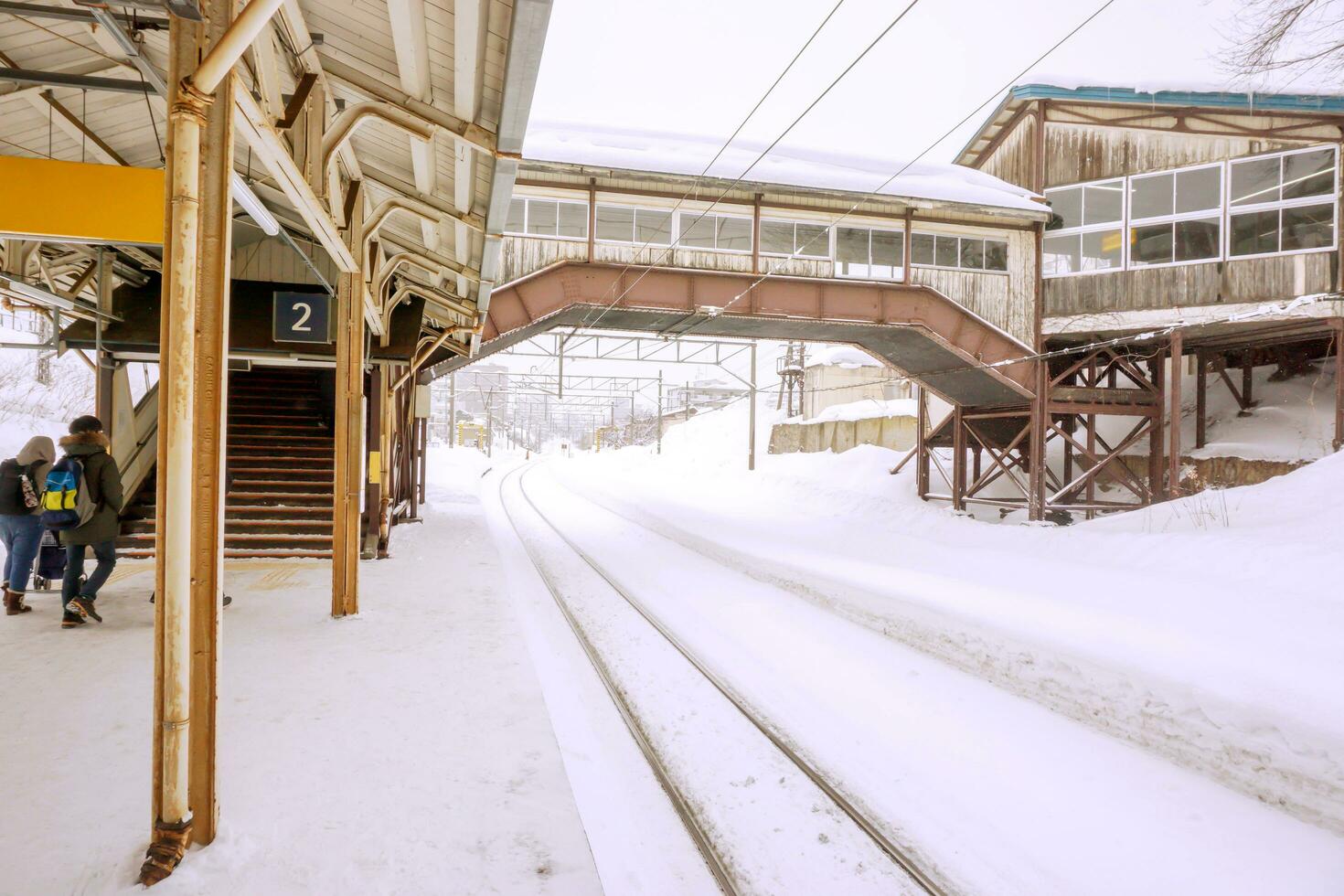 utanför se av hakodate gammal lokal- tåg stationens byggnader och metall lång järnväg Spår täckt förbi tjock snö i vinter- säsong vit dimmig bakgrund. foto