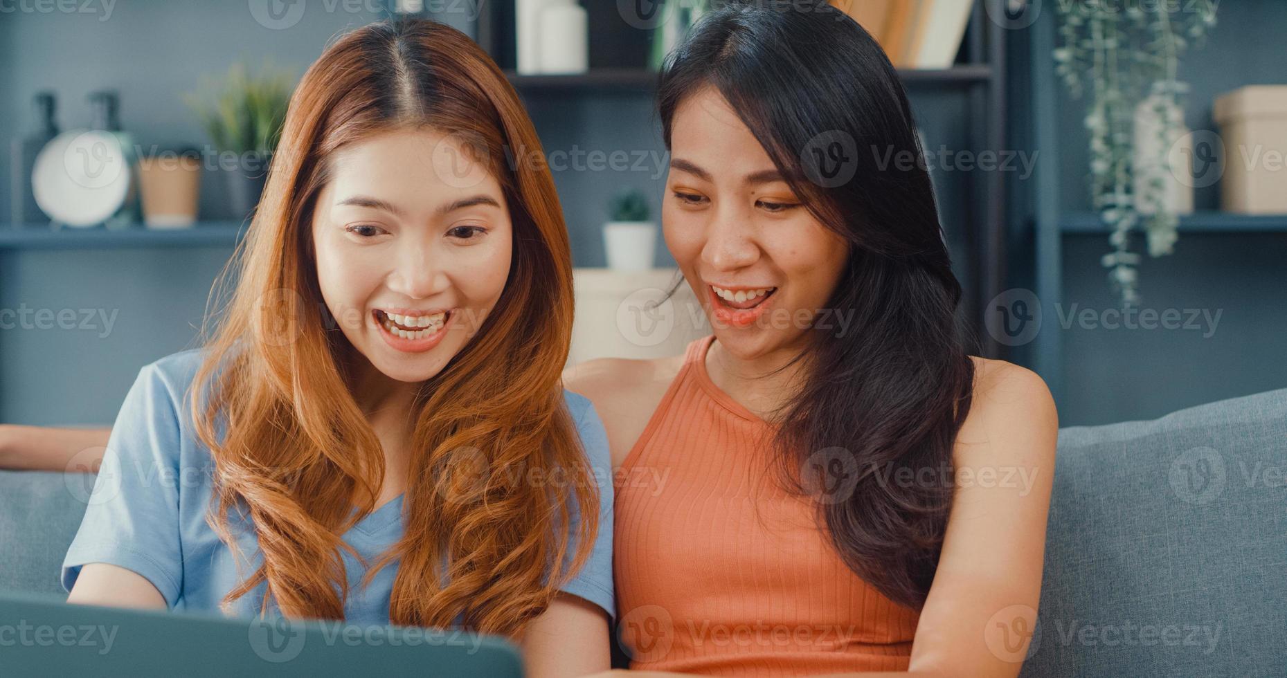 två asien lesbiska kvinnor webbplats på soffan tillsammans tittar på laptop skärm i vardagsrummet hemma tillsammans. lyckliga par rumskamrat damer njuta av webbsurfing online shopping, livsstil kvinna hemma koncept. foto