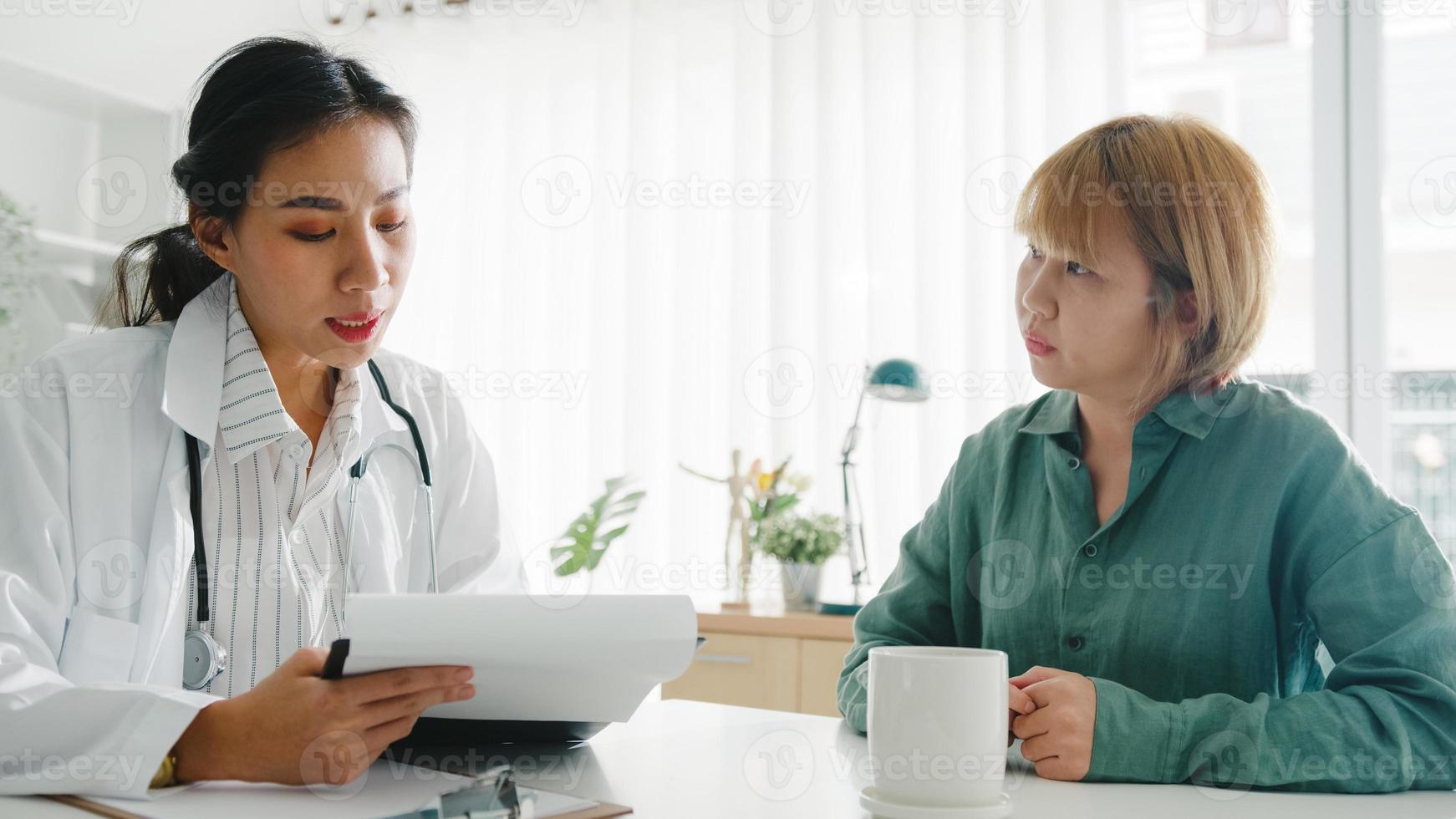 ung asiatisk kvinnlig läkare i vit medicinsk uniform med urklipp levererar bra nyheter prata diskutera resultat eller symptom med tjejpatient som sitter vid skrivbordet på vårdkliniken eller sjukhuskontoret. foto