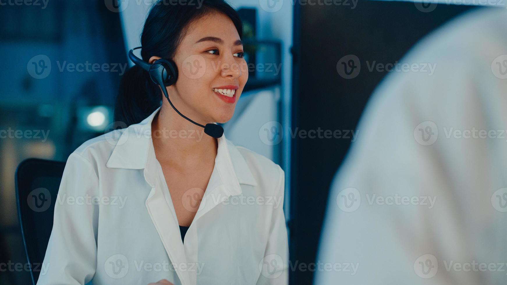 tusenåriga asien unga call center team eller kundsupport chef med hjälp av dator och mikrofon headset arbetar teknisk support på sena kvällen kontor. telemarketing eller försäljningsjobb koncept. foto