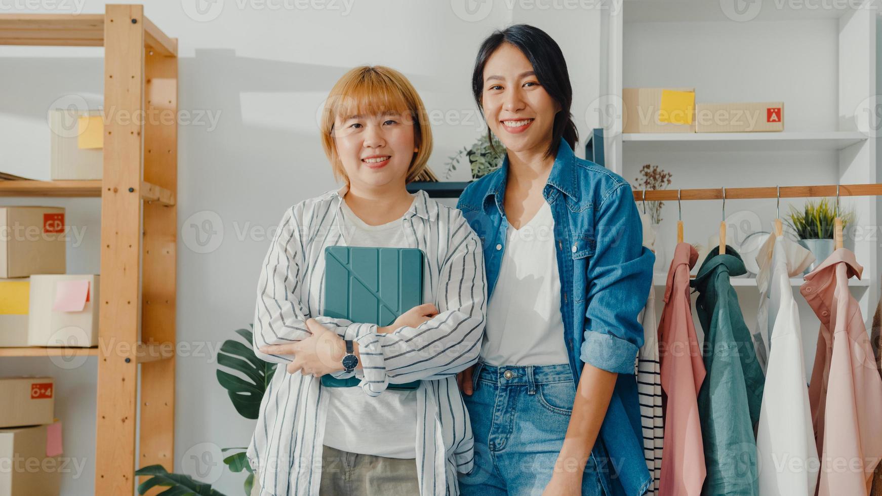 porträtt av unga asiatiska kvinnodesigner som känner ett lyckligt leende, korsade armar och ser till kameran medan du arbetar med klädbutik på hemmakontoret. småföretagare, online marknadsföringskoncept. foto