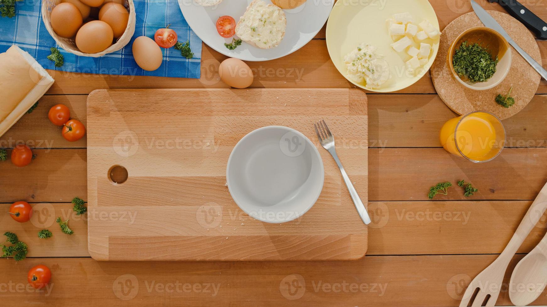 händer på ung asiatisk kvinna kock spricka ägg i keramisk skål koka omelett med grönsaker på träbräda på köksbordet hemma. livsstil hälsosam mat och traditionellt bagerikoncept. skott ovanifrån. foto