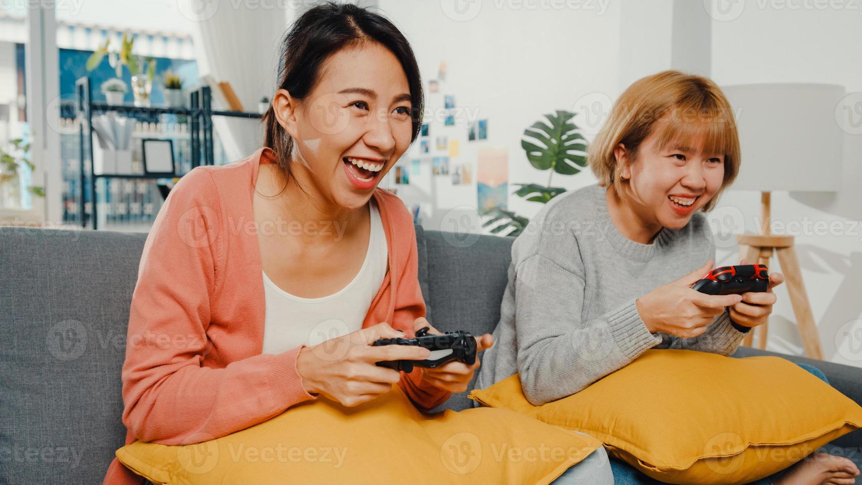 lesbisk lgbtq kvinnor par spela videospel hemma. ung asiatisk dam med trådlös handkontroll som har roligt lyckligt ögonblick tillsammans på soffan i vardagsrummet. de har en fantastisk och rolig tid firar semester. foto