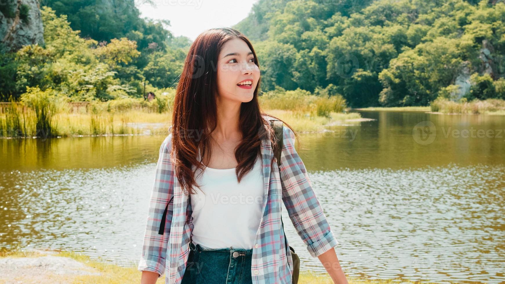 glad ung resenär asiatisk dam med ryggsäck som går vid fjällsjön. koreansk tonårsflicka njuta av sin semester äventyr känner glad frihet. livsstilsresor och koppla av i fritidskonceptet. foto