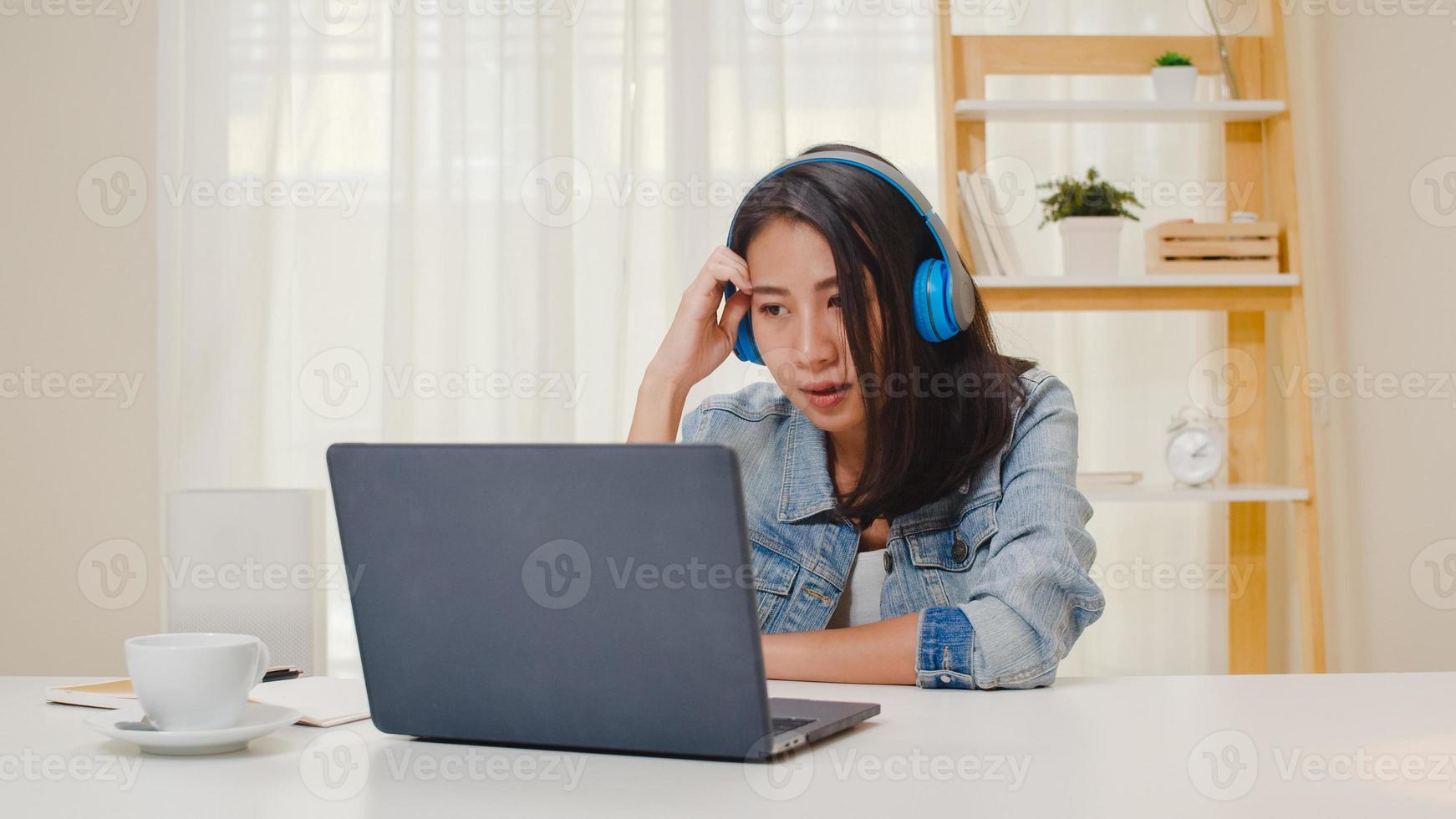 frilansande affärskvinnor fritidskläder med bärbar dator arbetar samtal videokonferens med kunden på arbetsplatsen i vardagsrummet hemma. glad ung asiatisk tjej koppla av sittande på skrivbordet gör jobbet på internet. foto