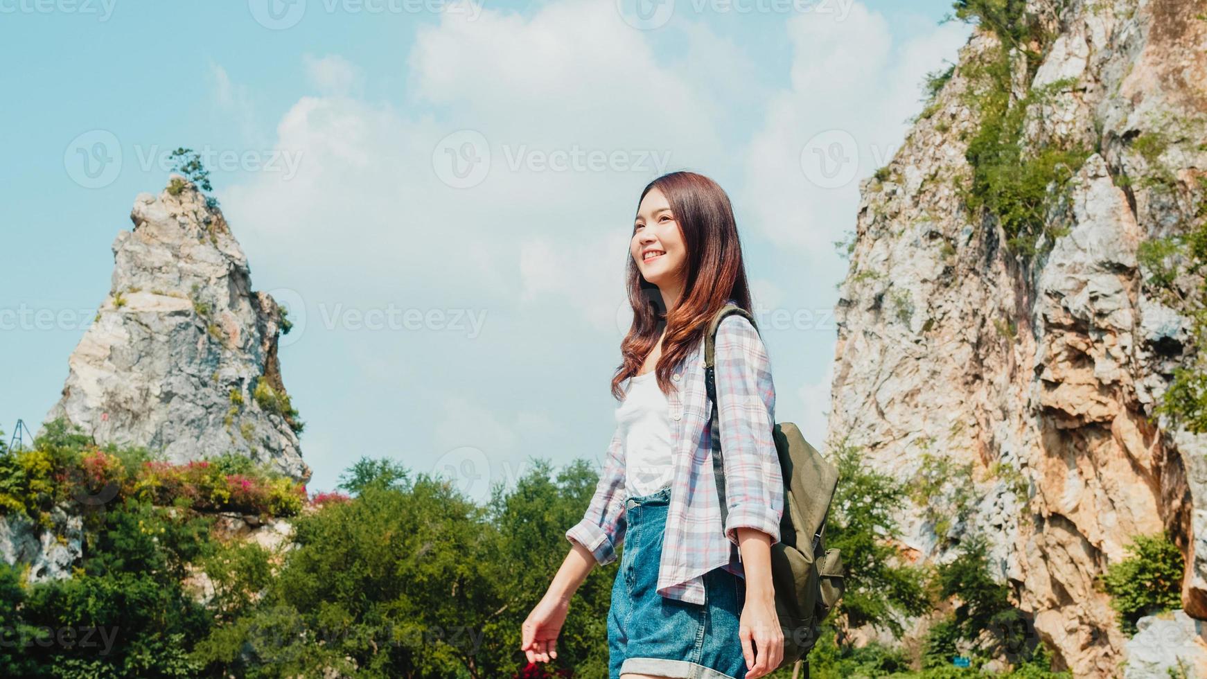 glad ung resenär asiatisk dam med ryggsäck som går vid fjällsjön. koreansk tonårsflicka njuta av sin semester äventyr känner glad frihet. livsstilsresor och koppla av i fritidskonceptet. foto