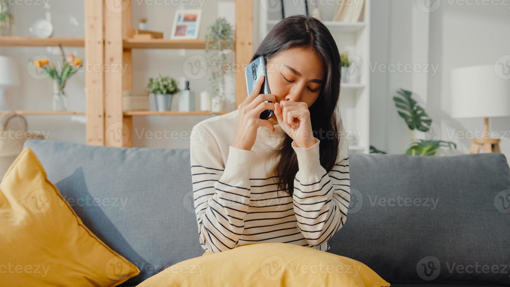 sjuk ung asiatisk kvinna hålla medicin sitta i soffan använda smartphone samtal för att rådgöra med läkare hemma. tjej tar medicin efter läkarorder, karantän hemma, socialt distanserat coronavirus -koncept. foto