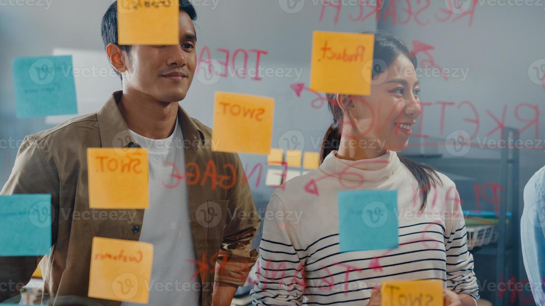 asiatiska affärsmän står bakom transparent glasvägg lyssnar chef pekar på framstegsarbete och brainstorm möte och arbetare post lappar på väggen på kontoret. affärsinspiration, dela idéer. foto