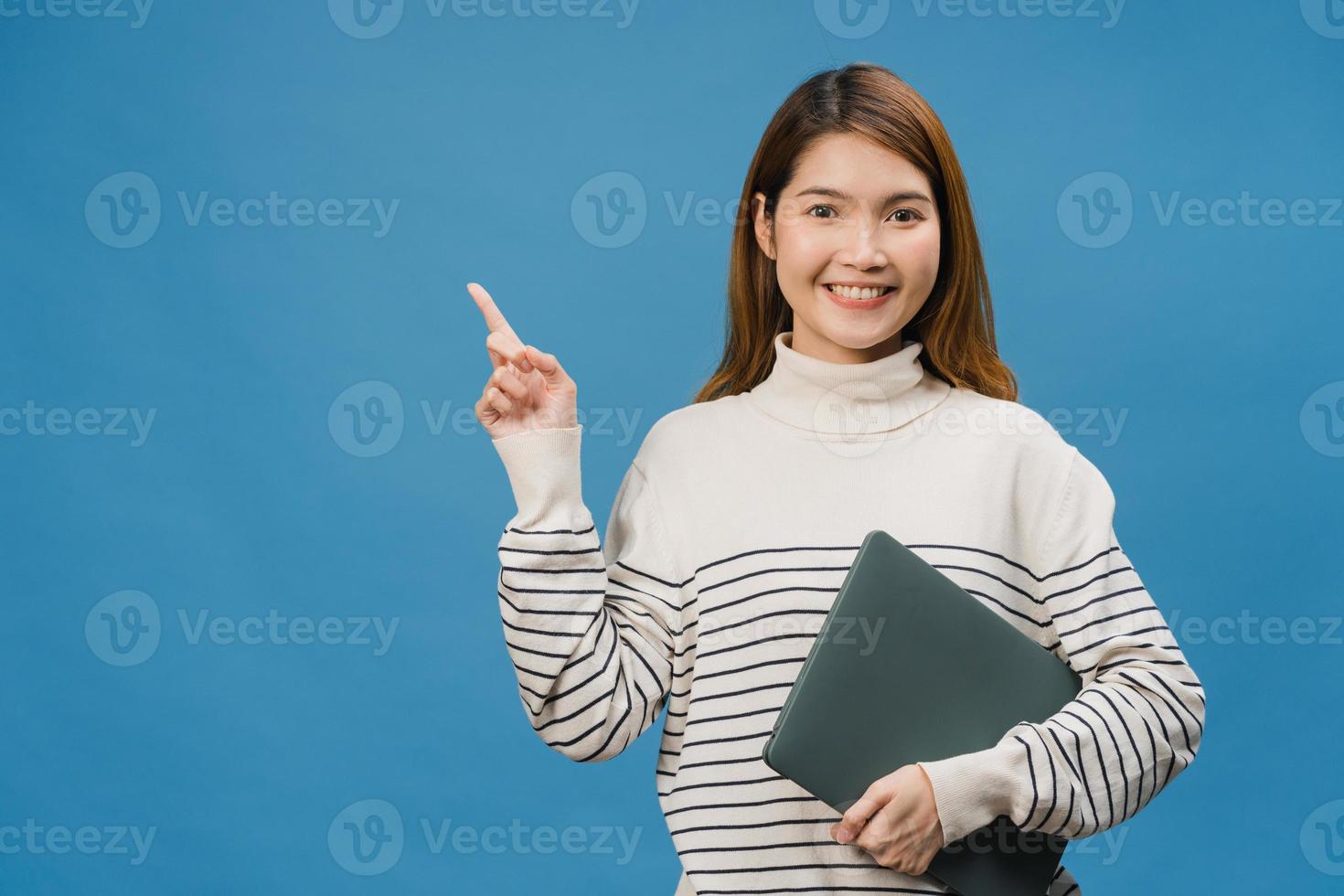 ung asiatisk dam som använder bärbar dator med positivt uttryck, ler brett, klädd i vardagskläder som känner lycka och står isolerad på blå bakgrund. glad förtjusande glad kvinna jublar över framgång. foto