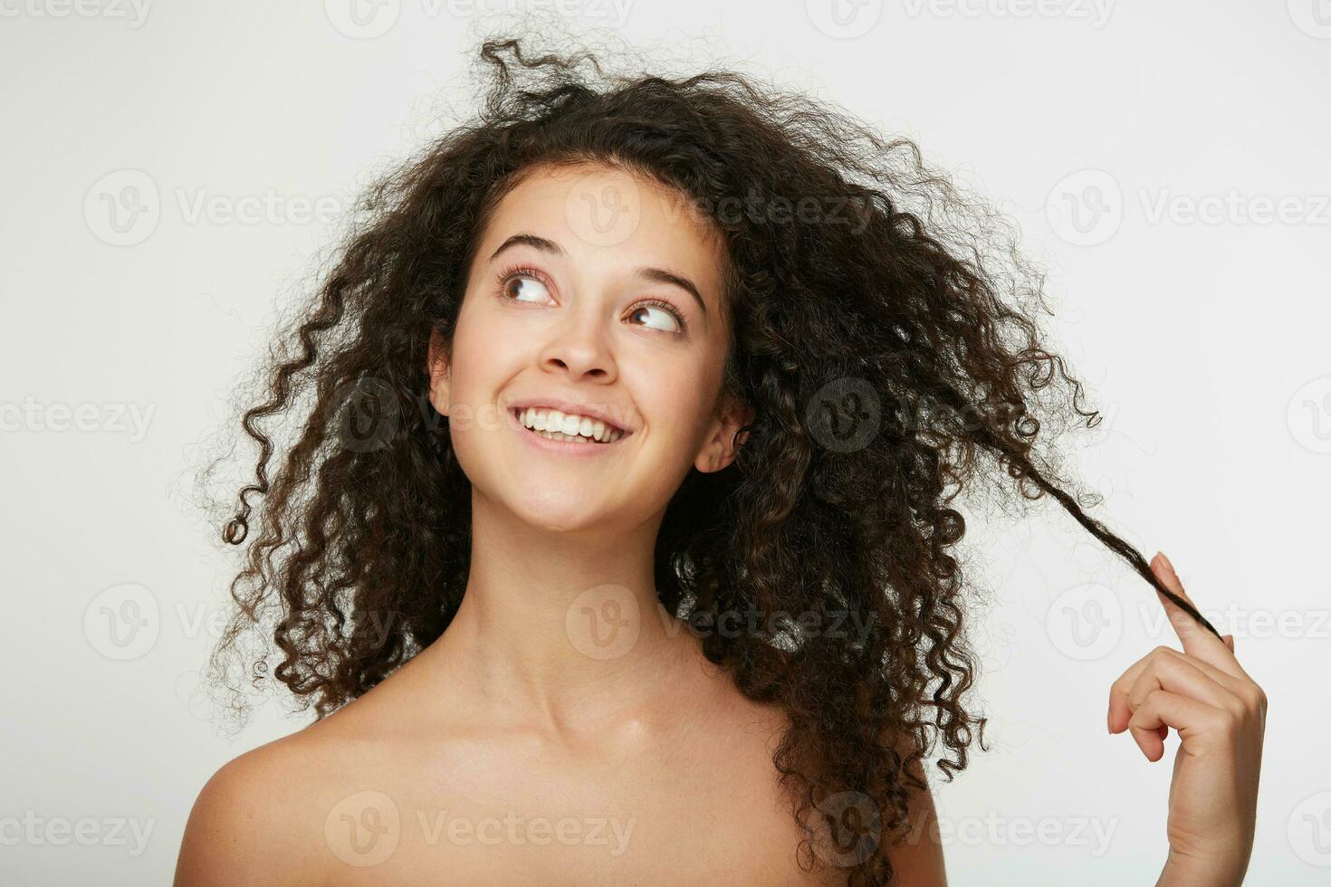porträtt av ett attraktiv charmig kvinna drömmande utseende bort och vindar skön lockigt hår på henne finger, flirtar, fint leende, huvud och axlar, över vit studio bakgrund foto