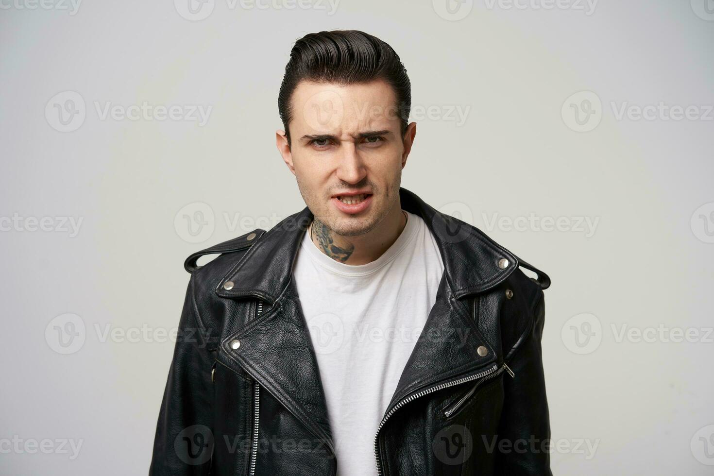 en ung motorcykel racer utseende arg, argumenterar, försvarar hans åsikt, ögonbryn rynkade, eldig ögon, mun på glänt, klädd i svart läder jacka, med en eleganta frisyr i fett, över vit bakgrund foto