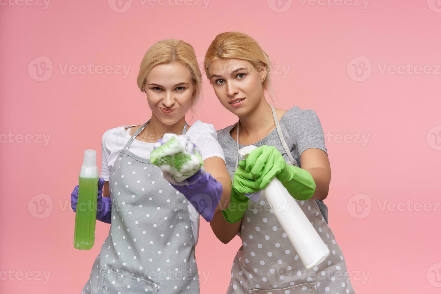 inomhus- Foto av ung vithuvud kvinnor med tillfällig frisyr innehav spray flaskor och svampar medan stående över rosa bakgrund i arbetssätt kläder