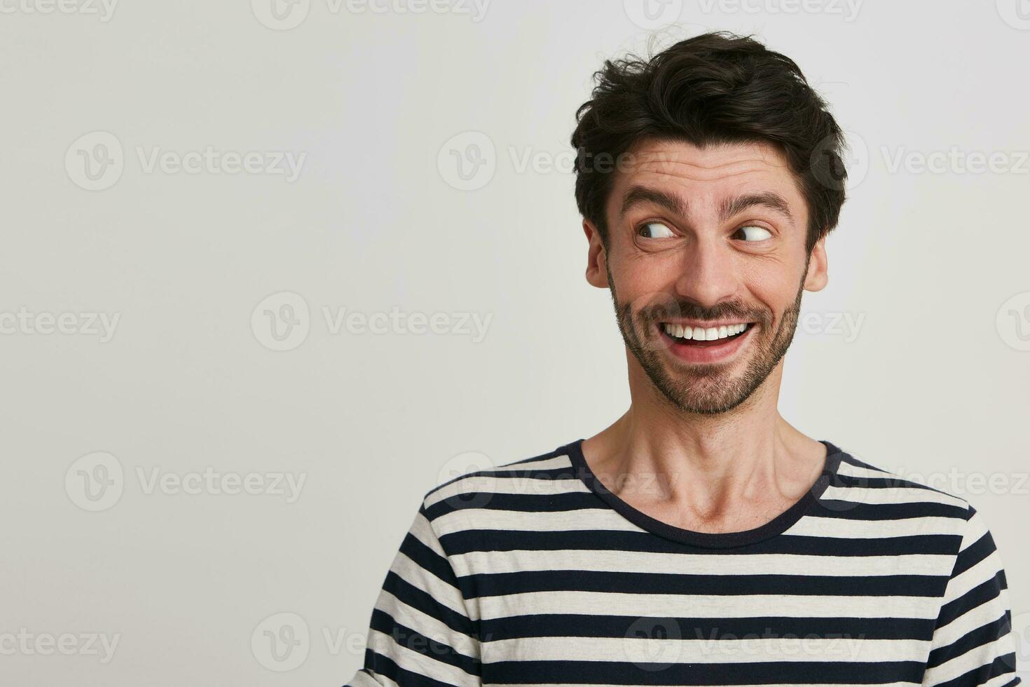porträtt av glad stilig skäggig ung man bär randig t skjorta leende och utseende till de sida isolerat över vit bakgrund foto