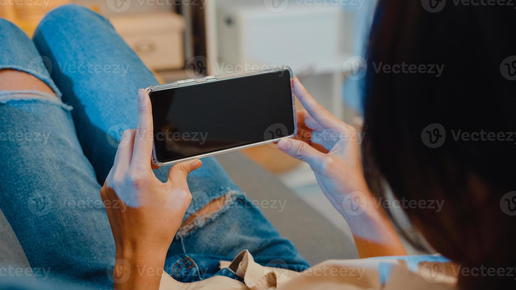 ung asiatisk dam använder smart telefon med tom svart skärm mock up display för reklam text medan vila på soffan i vardagsrummet på moderna hemmakväll. chroma key -teknik, marknadsföringskoncept. foto