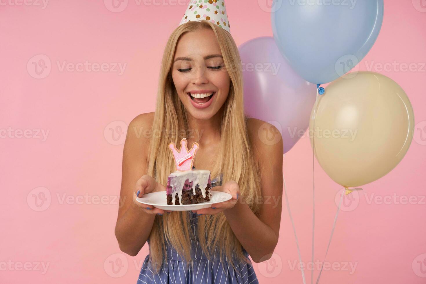 porträtt av glad ung lång håriga kvinna bär blå sommar klänning fira Semester, Framställ i flerfärgad luft ballonger med födelsedag kaka, isolerat över rosa bakgrund foto