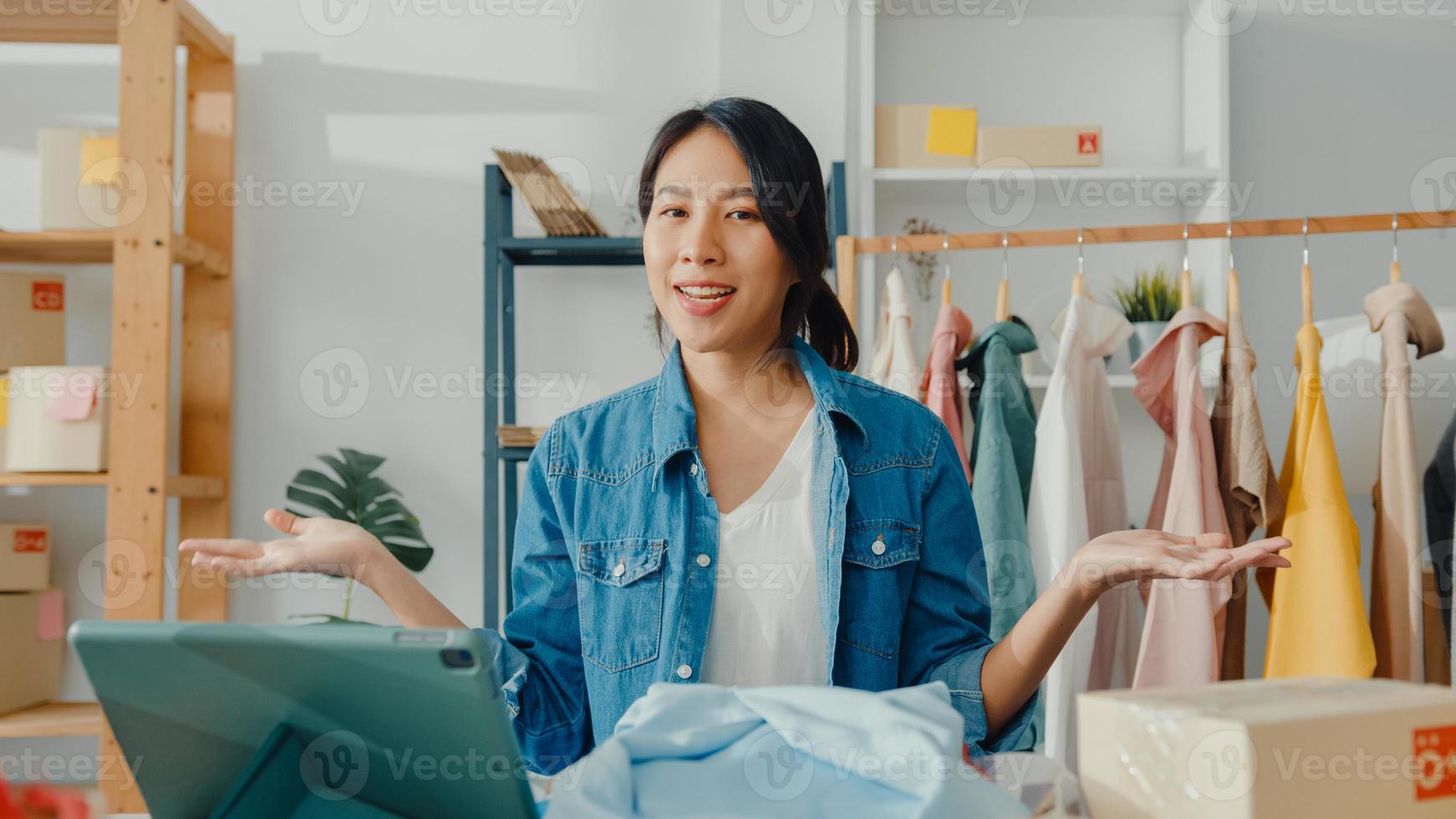 ung asiatisk dammodedesigner som använder mobiltelefon tar emot inköpsorder och visar kläder som spelar in video live streaming online i butik. småföretagare, online marknadsföringskoncept. foto