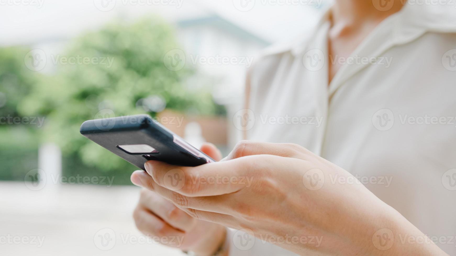 attraktiv ung asiatisk affärskvinna som använder mobiltelefon som kontrollerar sociala medier internet, chattar med vänner utanför på gatan i staden. livsstil ny normal efter coronavirus och social distansering. foto