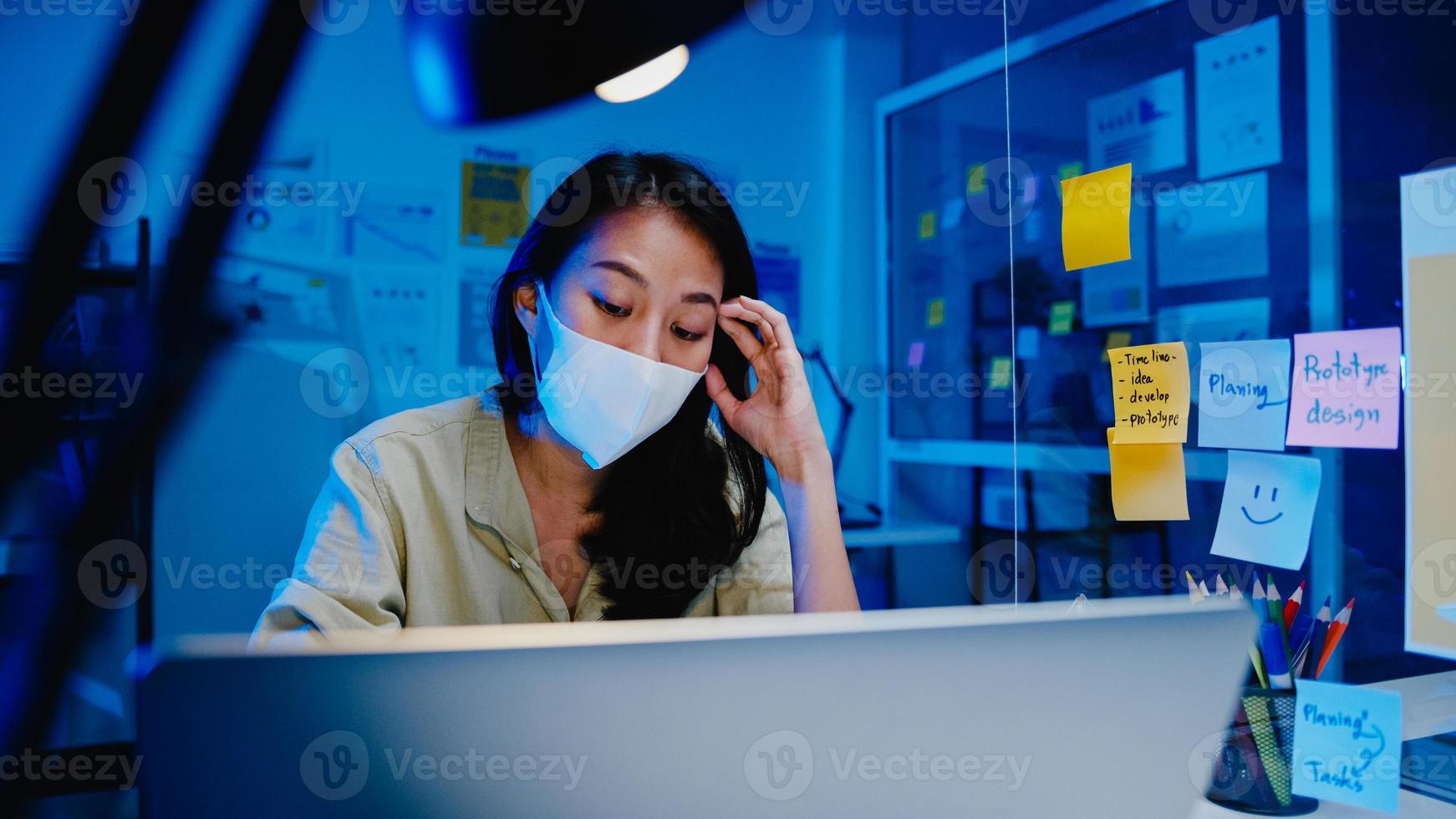 frilansande asiatiska kvinnor bär ansiktsmask med hjälp av laptop hårt arbete på nytt vanligt kontor. arbeta hemifrån överbelastning på natten, självisolering, social distansering, karantän för förebyggande av coronavirus. foto