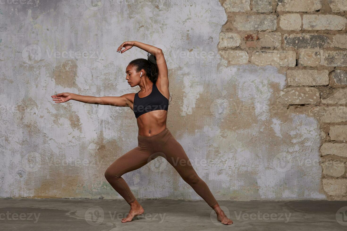 främre full längd Foto av flexibel modern dansare övar i dansa studio, rör på sig med musik i henne hörlurar, bär bekväm sportig kläder över loft interiör