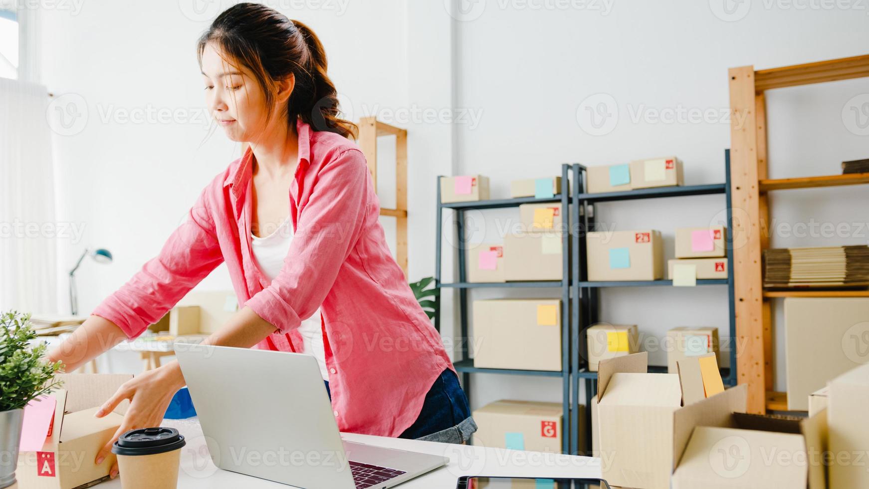 ung asien entreprenör affärskvinna kontrollera produkt inköpsorder på lager och spara till dator laptop arbete på hemmakontor. småföretagare, onlinemarknadsleverans, livsstil frilansande koncept. foto