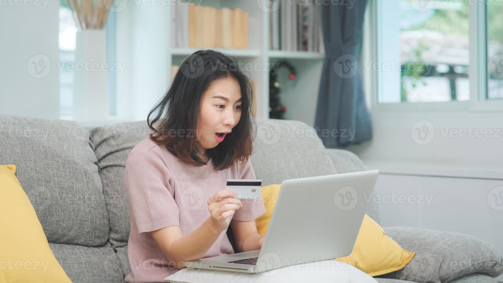 asiatisk kvinna som använder bärbar dator och kreditkort shopping e -handel, kvinnliga koppla av känner sig glad online shopping sitter på soffan i vardagsrummet hemma. livsstil kvinnor slappna av hemma koncept. foto