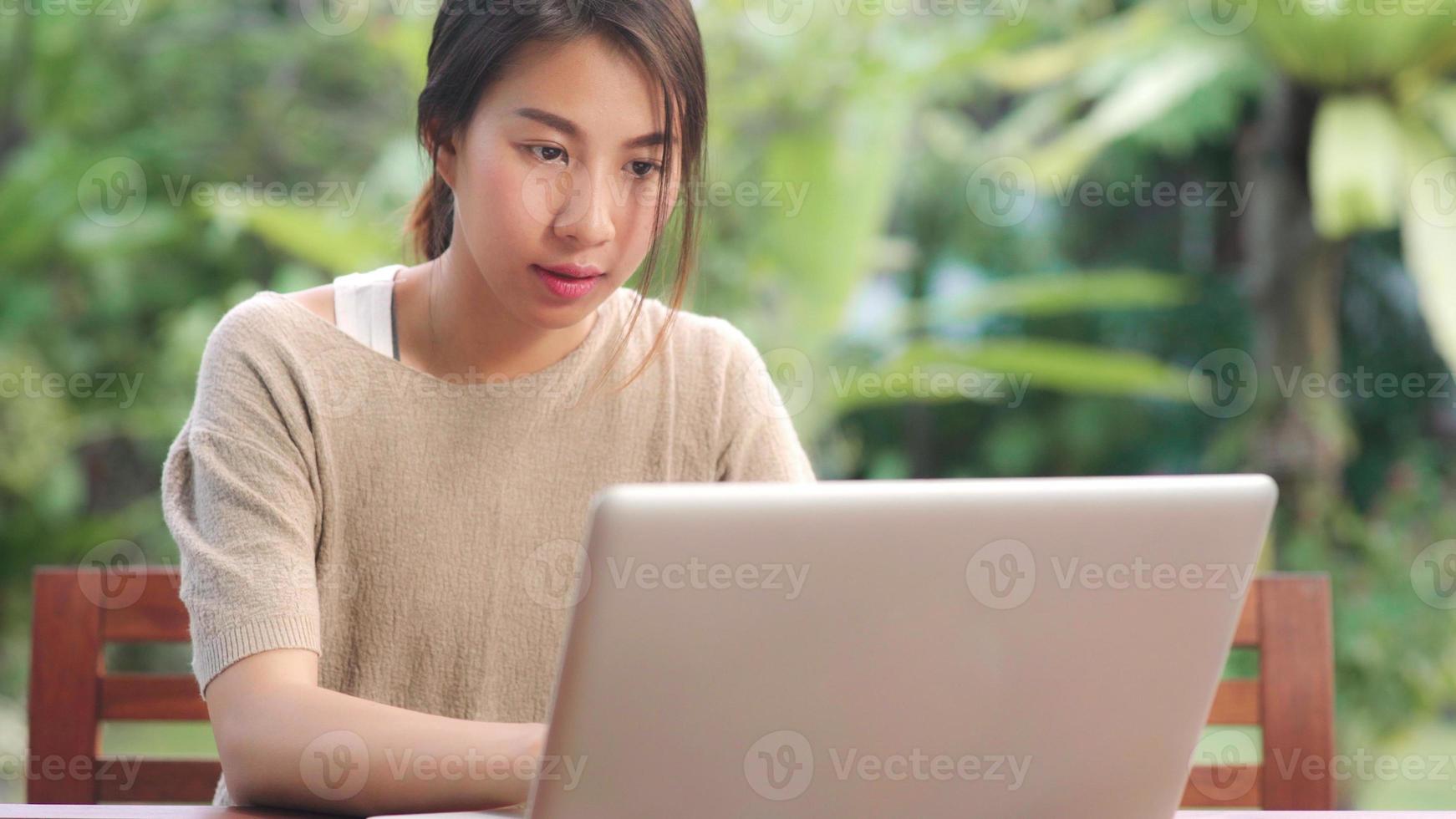 frilans asiatisk kvinna som arbetar hemma, affärskvinna som arbetar på bärbar dator sitter på bordet i trädgården på morgonen. livsstil kvinnor arbetar hemma koncept. foto