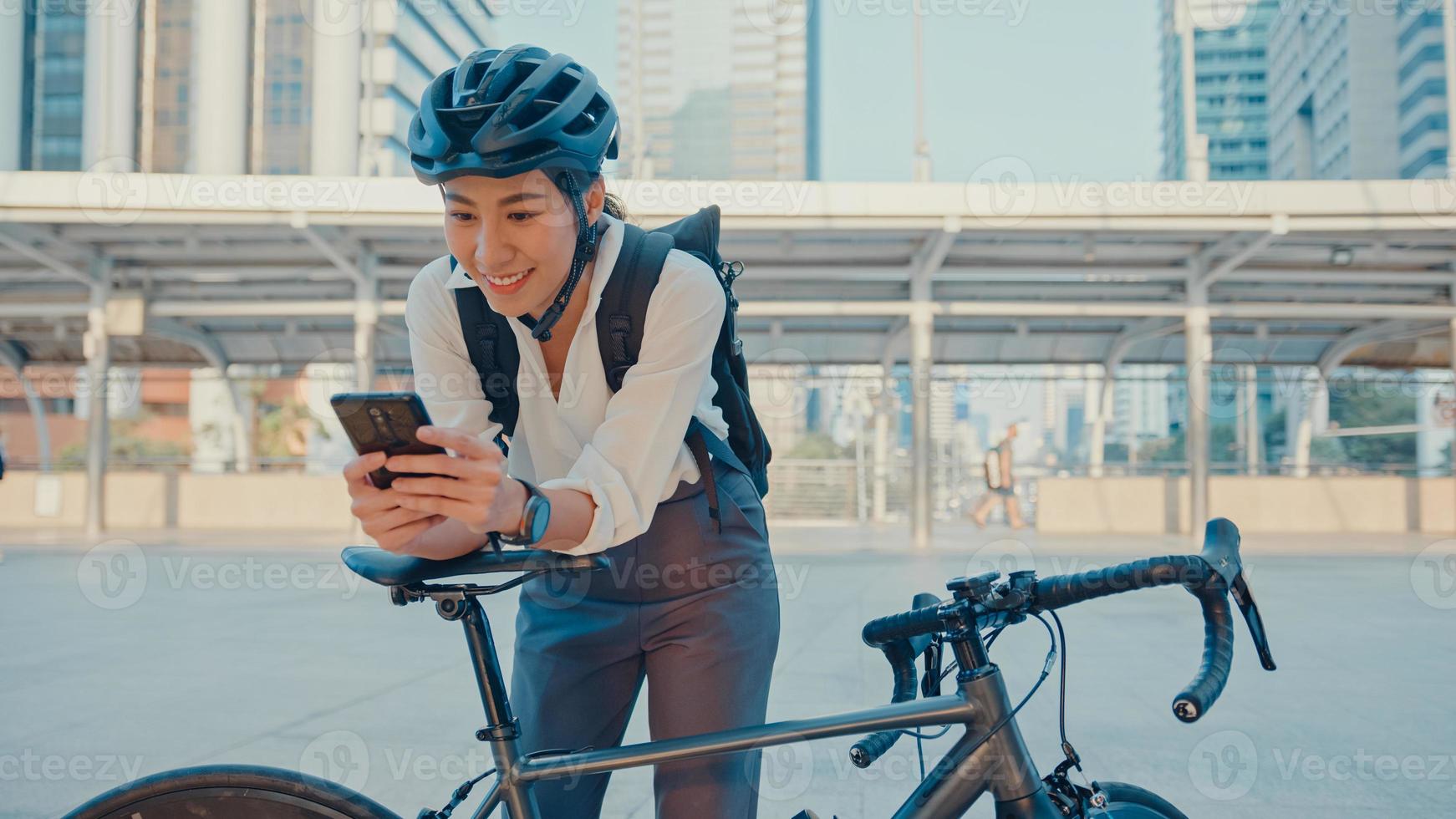 le asiatisk affärskvinna med ryggsäck använda smart telefon titta kamera i stad stå på gatan med cykel gå till jobbet på kontoret. sportflicka använder telefonen för arbete. pendla till jobbet, affärspendlare i staden. foto