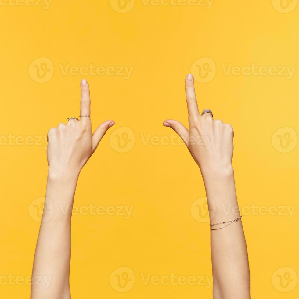studio Foto av Söt kvinna Uppfostrad händer med prydnadsväxter som visar uppåt med index fingrar medan varelse isolerat över gul bakgrund. tecken och gester begrepp