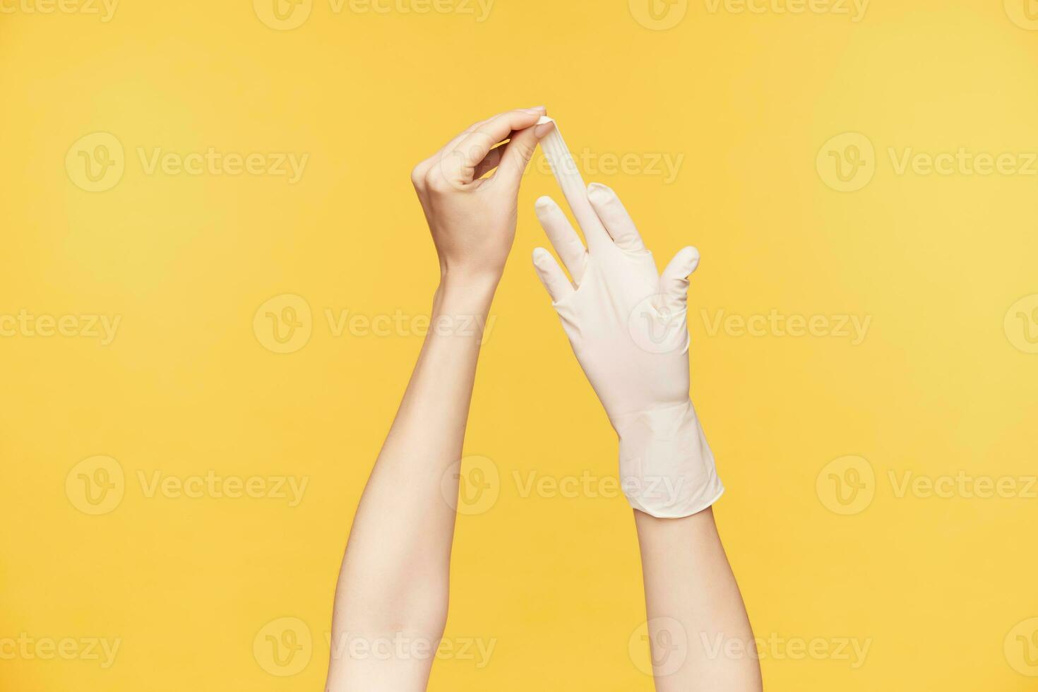 inomhus- skott av ung ljushyad kvinnas hand dragande vit handske från Övrig hand med mitten finger, isolerat över orange bakgrund. mänsklig händer begrepp foto