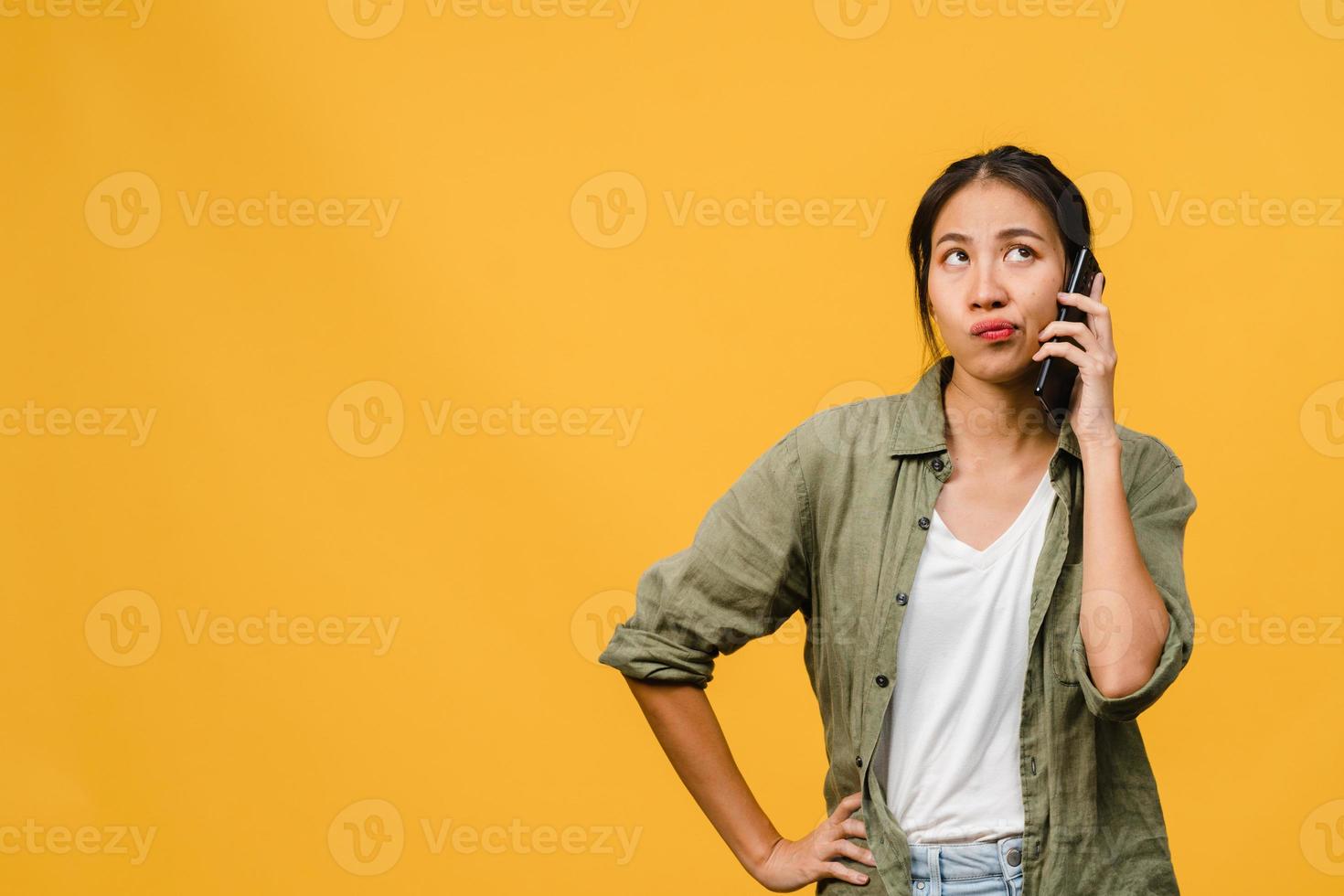 ung asiatisk dam pratar i telefon med negativt uttryck, upphetsad skrik, gråter känslomässigt arg i avslappnad trasa och står isolerad på gul bakgrund med tomt kopieringsutrymme. ansiktsuttryck koncept. foto