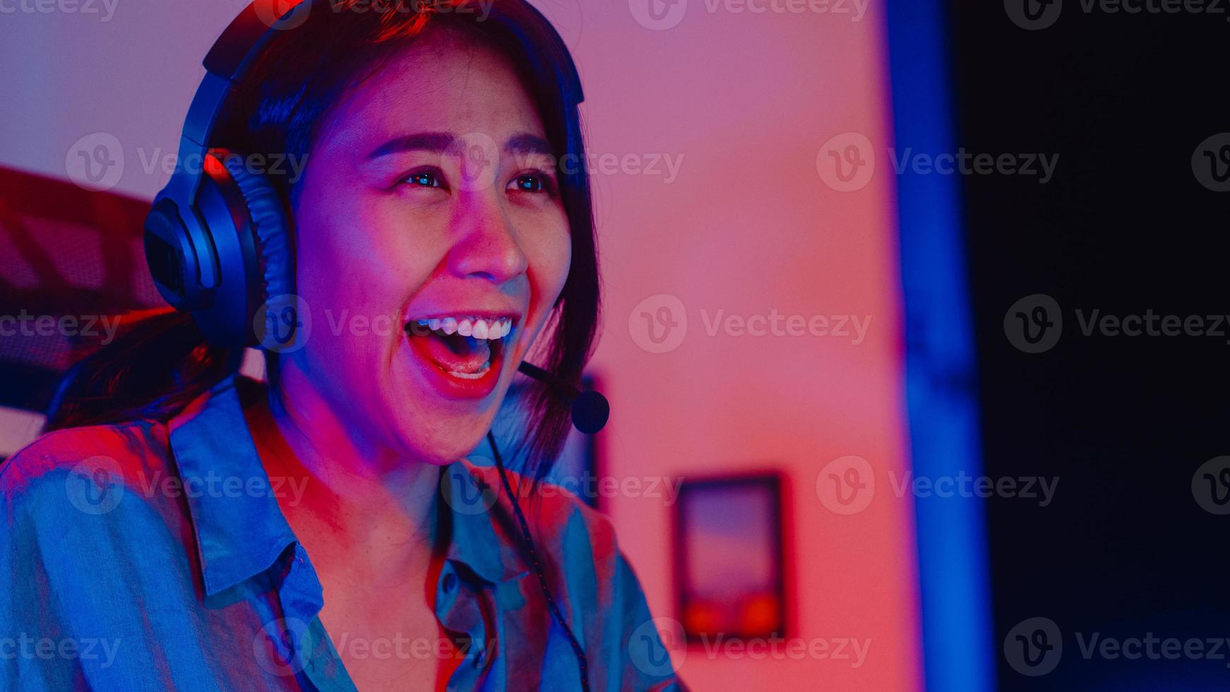 närbild ansikte glad asien professionell tjej spelare bära hörlurar tävling spela videospel neonljus dator i vardagsrummet hemma. esport -strömmande spel online, hemmakarantänaktivitetskoncept. foto