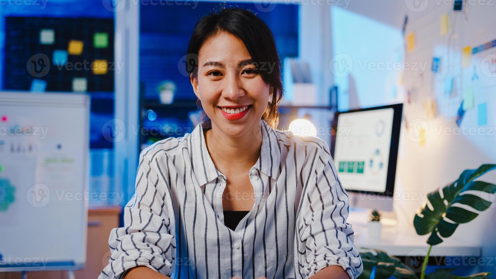 porträtt av vacker verkställande affärskvinna smart vardagskläder som tittar på kameran och ler, glad i modern kontorsarbetsplats natt. ung asiatisk dam prata med kollega i videosamtalsmöte hemma. foto