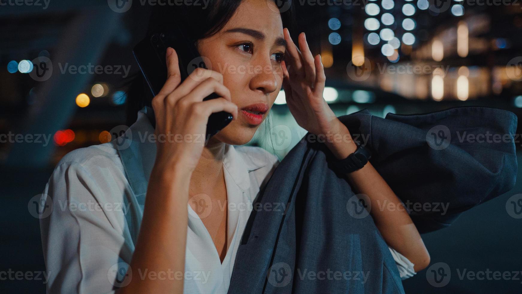 allvarligt missnöjd upprörd ung asiatisk affärskvinna som pratar via telefon medan hon går ensam utomhus i stadens stadskväll. företag på gång, social distansering för att förhindra spridning av covid-19-konceptet. foto