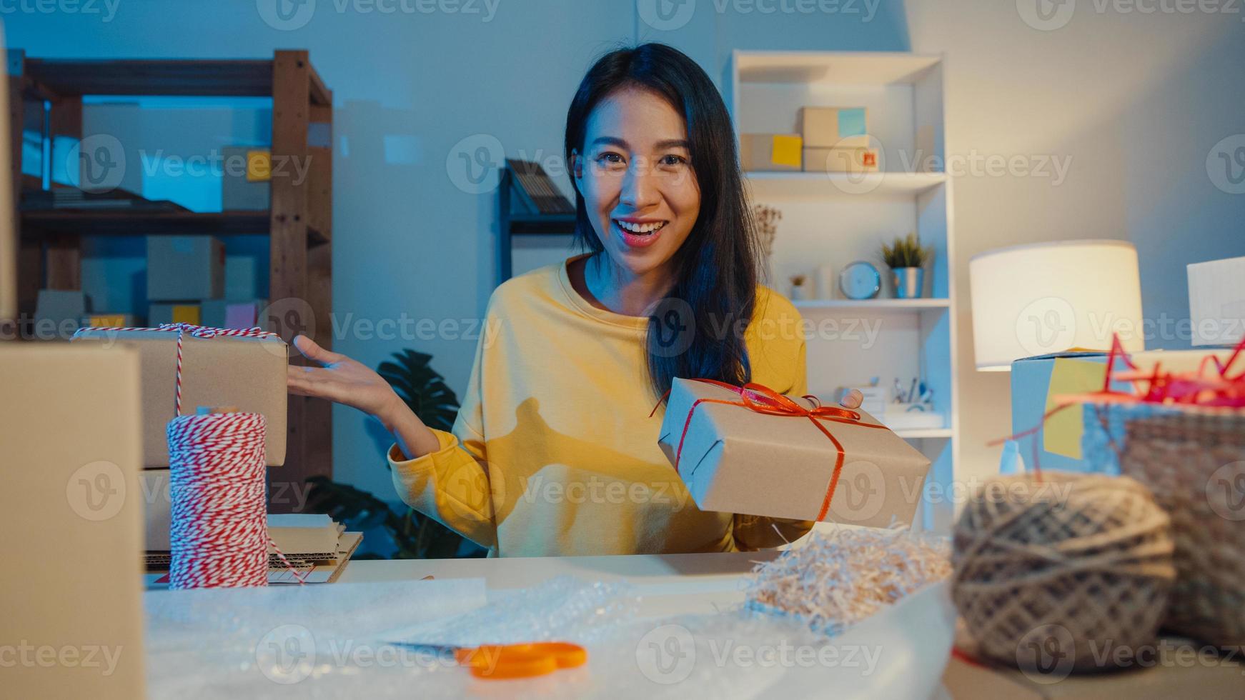 glad ung asiatisk affärskvinna som tittar på kamerasäljning introducerar produkt till klientvideo livestreaming på nätbutiksmarknaden på natten. småföretagare, online marknadsföringskoncept. foto