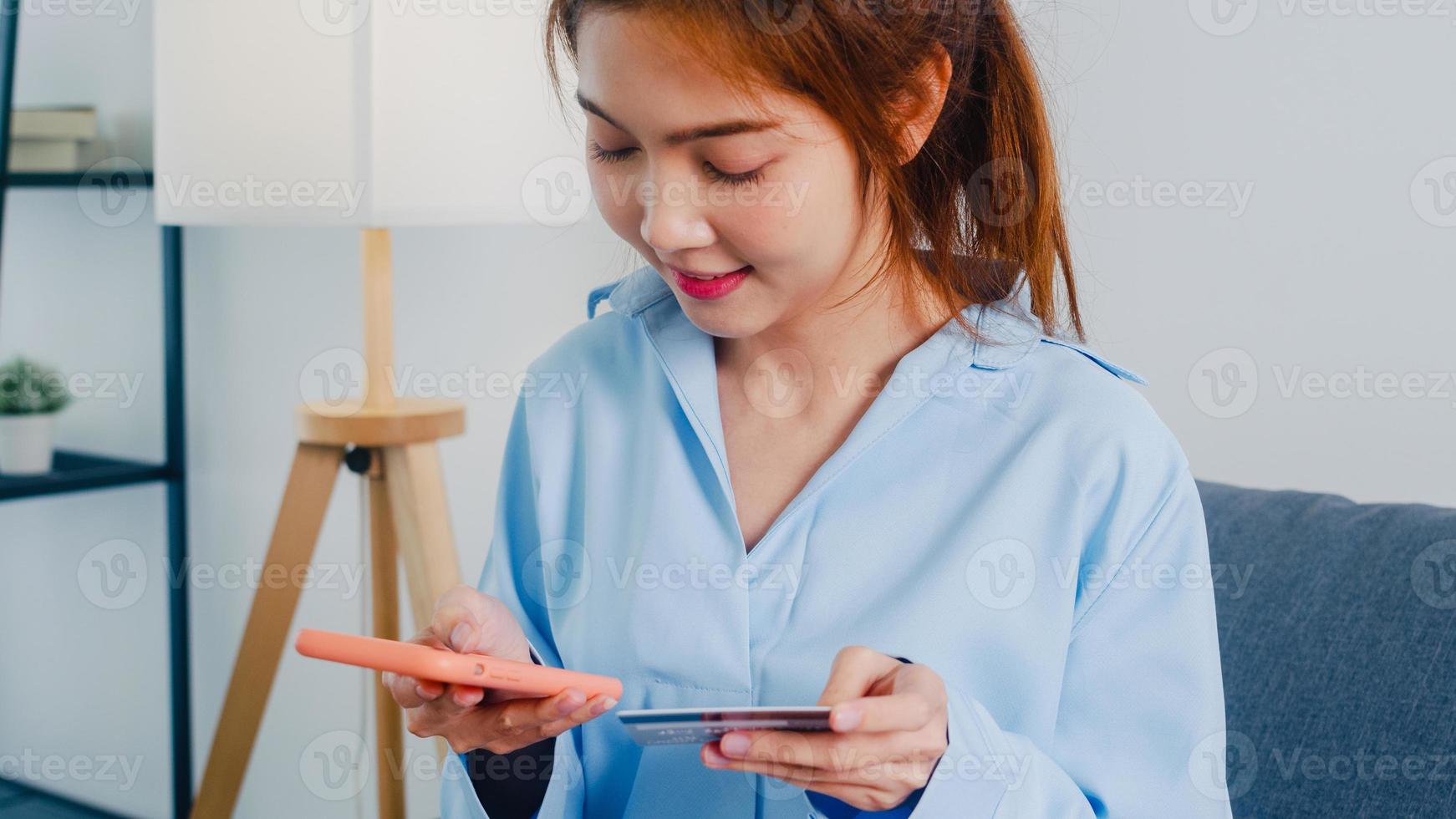 ung asiatisk dam använder smart telefon, kreditkort köper och köper e-handel internet i vardagsrummet hemma. stanna hemma, shoppa online, självisolering, social distans, karantän för coronavirus. foto