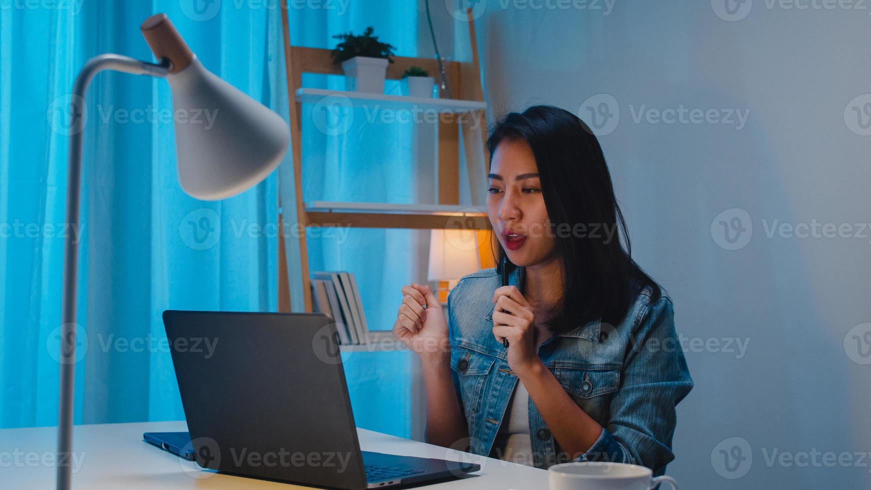 frilans smarta affärskvinnor som lyssnar musik efter användning laptop arbetar hårt på arbetsplatsen i vardagsrummet hemma på natten. glad ung asiatisk tjej som sitter på skrivbordet jobbar övertid, dans njut av avkopplingstid. foto