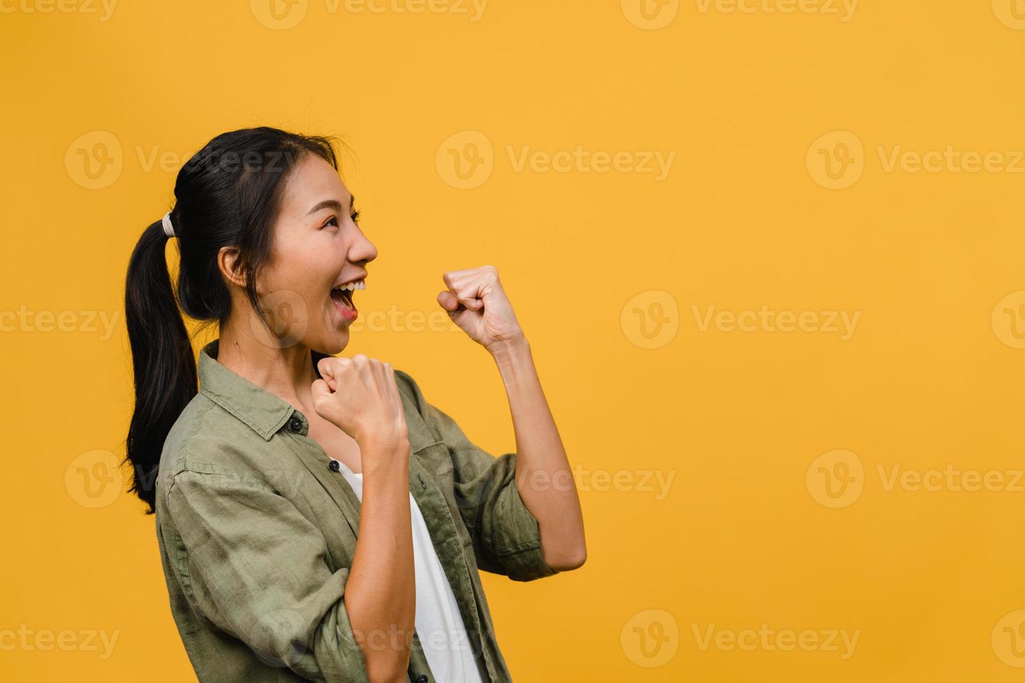 ung asiatisk dam med positivt uttryck, glad och spännande, klädd i avslappnad trasa över gul bakgrund med tomt utrymme. glad förtjusande glad kvinna jublar över framgång. ansiktsuttryck koncept. foto