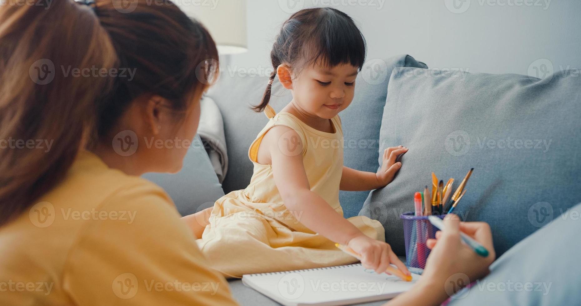 glad glad Asien familj mamma lära flicka måla använda album och färgglada pennor ha kul koppla av på soffan i vardagsrummet hemma. umgås tillsammans, social distans, karantän för coronavirus. foto