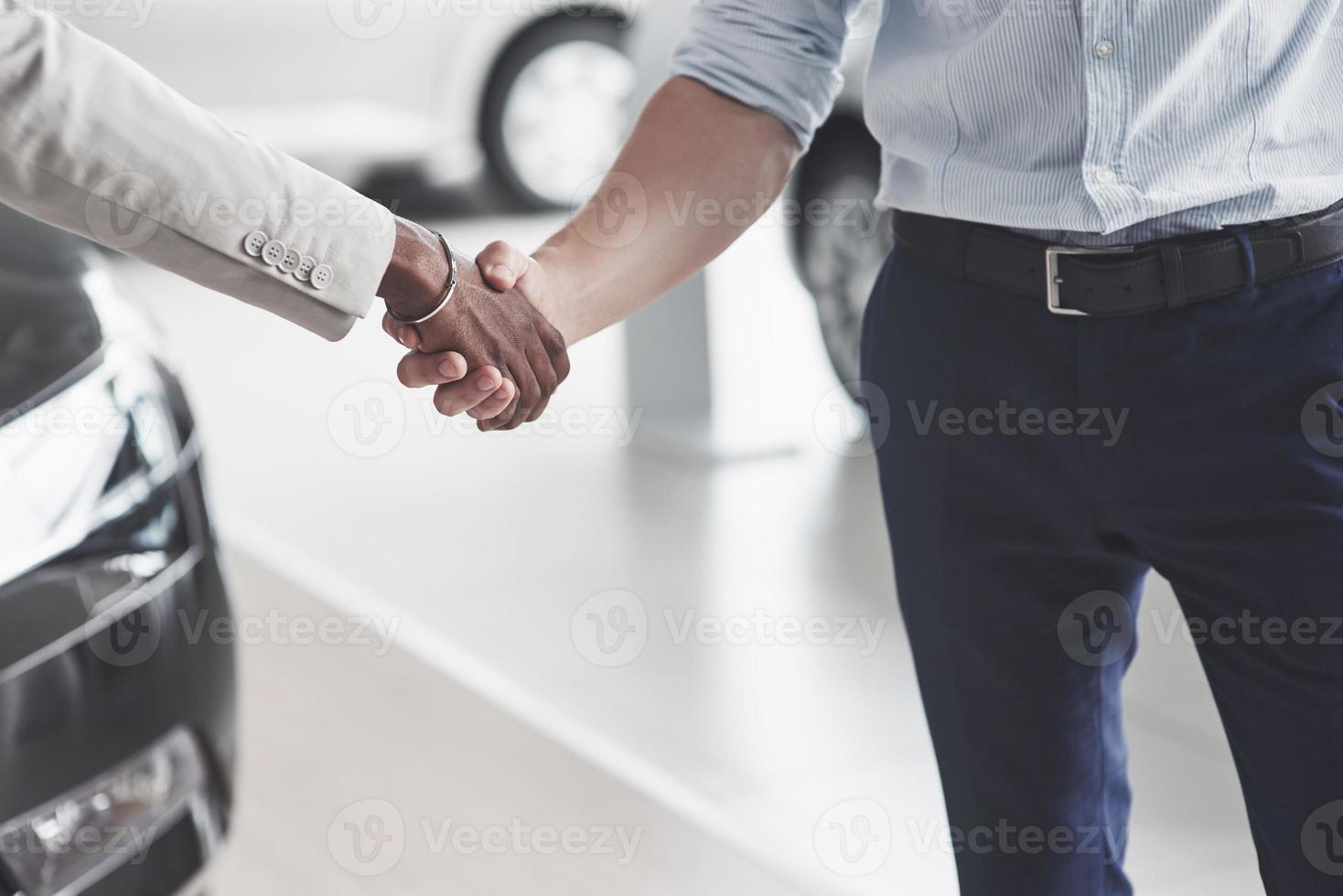 närbild av säljare, rör sig i händerna med en manlig afrikansk kund efter försäljningen av en ny bil. foto